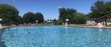 Uma piscina com água azul cristalina, rodeada por árvores e um edifício com telhado vermelho.