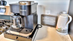 Una cafetera Keurig sobre una encimera de cocina, con una taza de café y un marco con una cita sobre el café.