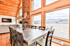 A dining area with a wooden table and chairs, a fireplace, and large windows with a view of mountains.