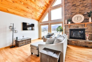 Una sala de estar con techo de madera, chimenea, televisor y sofá.
