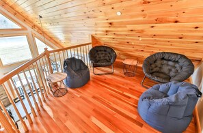 A wooden interior with a wooden staircase, a view through a window, and three bean bag chairs.
