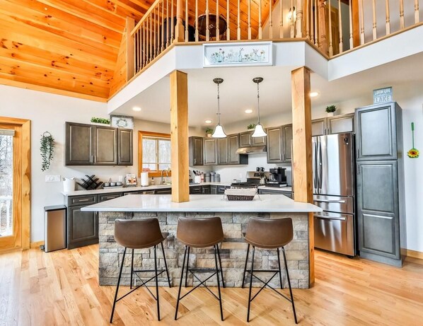 A spacious kitchen with a large island, bar stools, and a view of a lake.