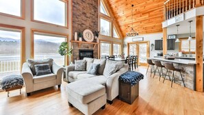 A spacious living room with a large sectional sofa, a fireplace, and a kitchen area with bar stools. - Lakeside Catskills Escape • Soak, Sip & Stargaze (Cairo)