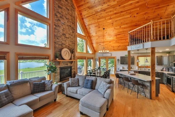 Amplia sala de estar con chimenea, cocina con barra y vista a un lago.