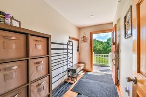 A hallway with storage cabinets, a metal rack, a bench, and a door leading to a balcony with a view of greenery.