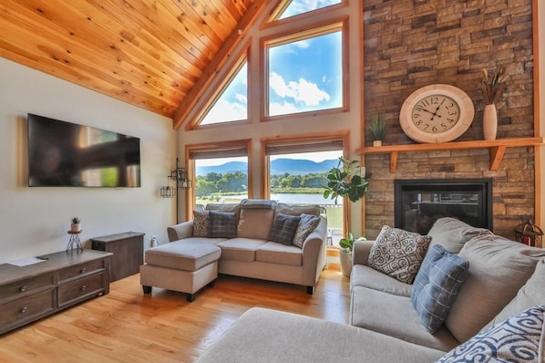 Un salón amplio con chimenea, ventanas grandes y un televisor de pantalla plana.
