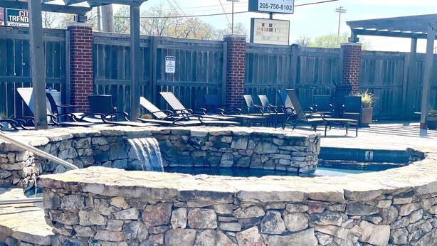 Una piscina de piedra con cascada, rodeada de sillones de descanso y una valla de madera.