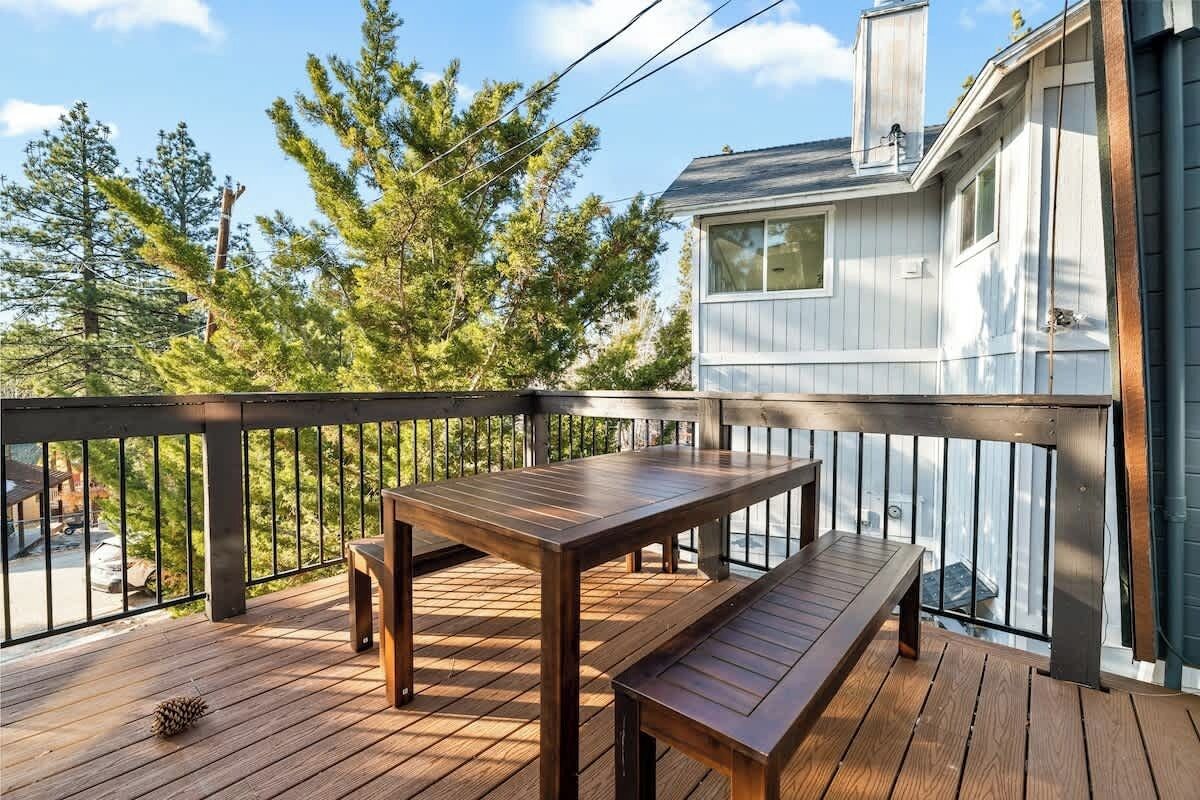 A wooden deck with a table and bench, overlooking a house with a window and a chimney.