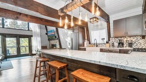 Een moderne keuken met een groot eiland, houten krukken en een backsplash van visgraatmozaïek.