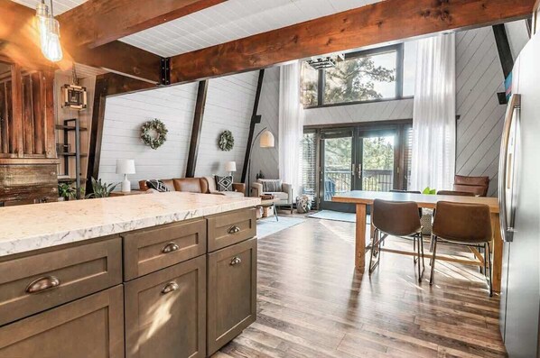 A kitchen with a large island, wooden beams, and a dining area with chairs.
