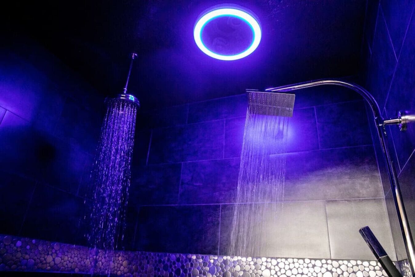 Une salle de bain moderne avec un luminaire circulaire, un élément décoratif vertical avec de l’eau et une pomme de douche.