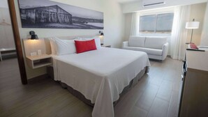 A hotel room with a large bed, a sofa, a desk, and a window with a view.
