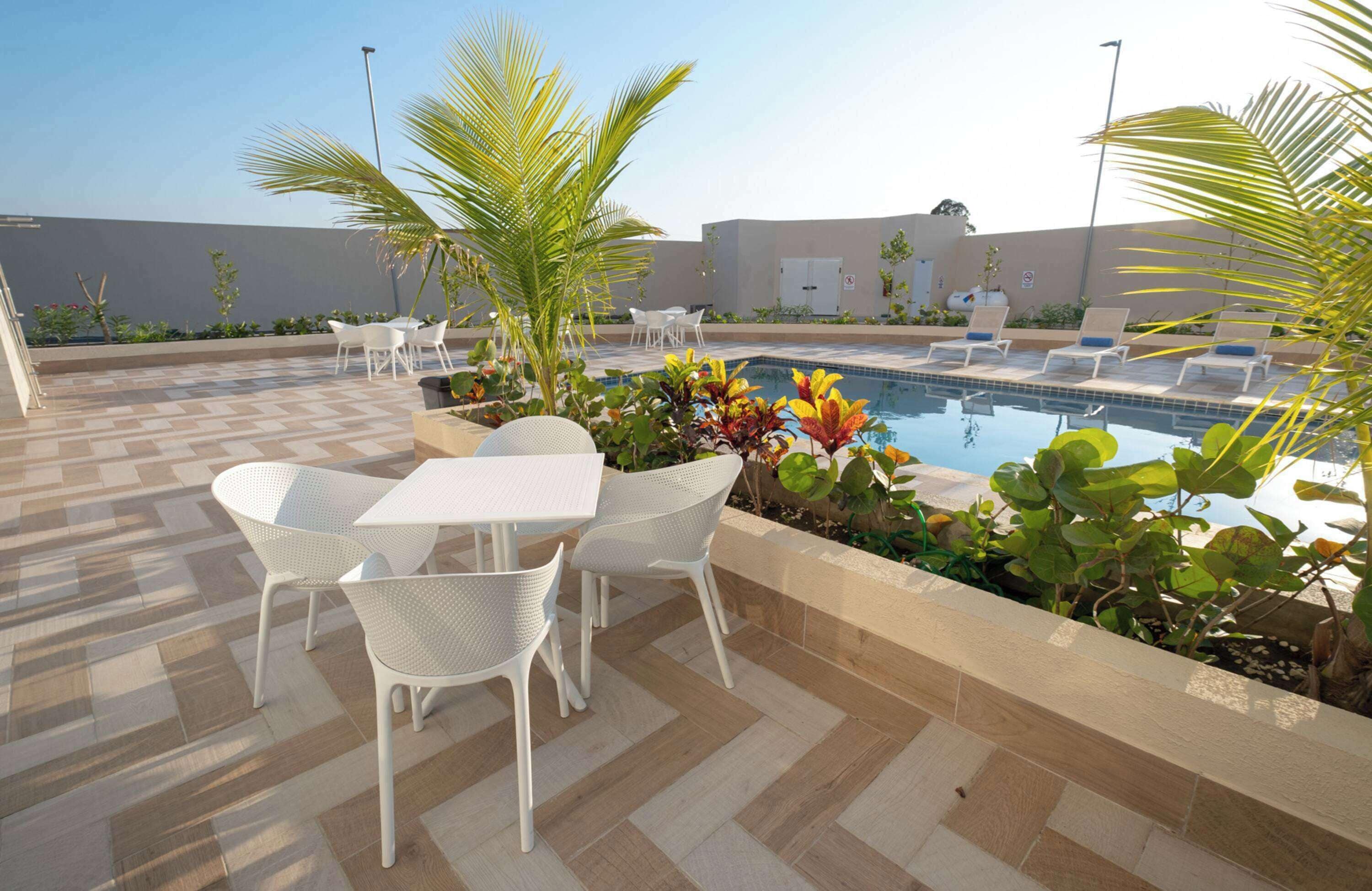 Zona de piscina amb terra de pissos, seients de relaxació blancs i una piscina.