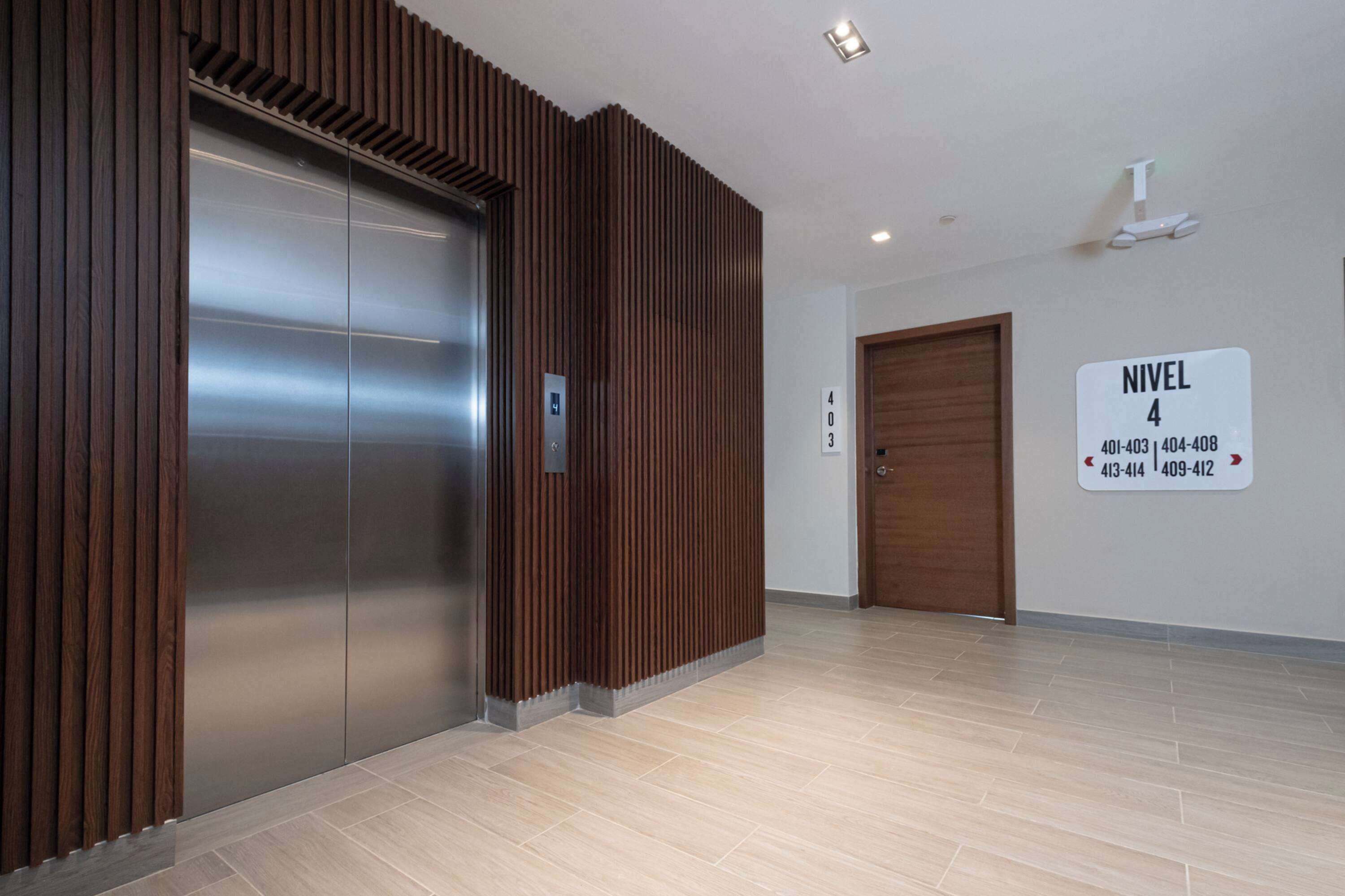 A modern elevator with a wooden panel design, a sign indicating 'NIVEL 4' with floor numbers, and a clean, tiled floor.