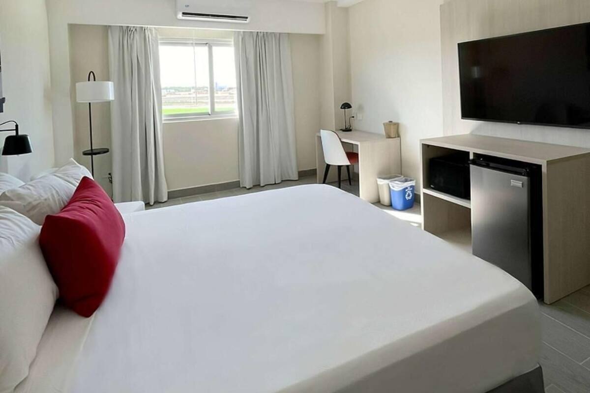 Une chambre d’hôtel avec un lit, un bureau, une télévision et une fenêtre avec des rideaux.