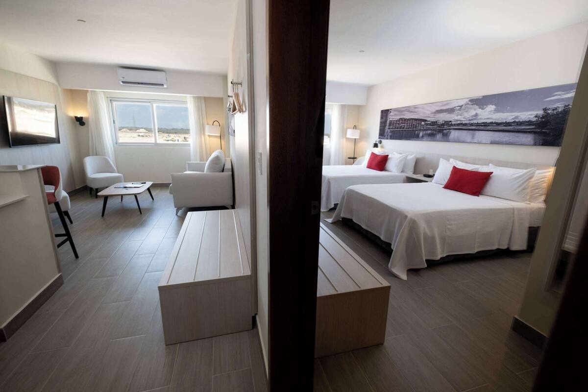 Une chambre d’hôtel avec deux lits, un bureau, une chaise, un canapé et une grande fenêtre donnant sur un beau paysage.