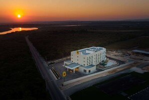 A modern building with a central courtyard and a swimming pool, surrounded by open fields and a road. - Super 8 By Wyndham Manzanillo (Pepillo Salcedo)
