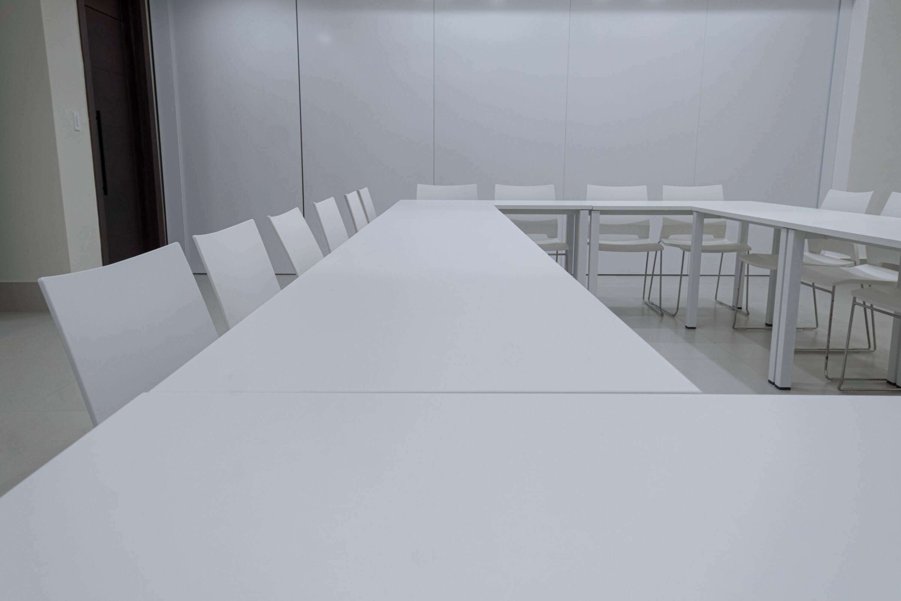Uma sala de conferências com uma mesa branca comprida e várias cadeiras brancas.