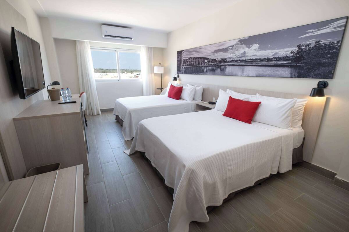 Une chambre d’hôtel avec deux lits, une télévision, un bureau et une grande fenêtre.