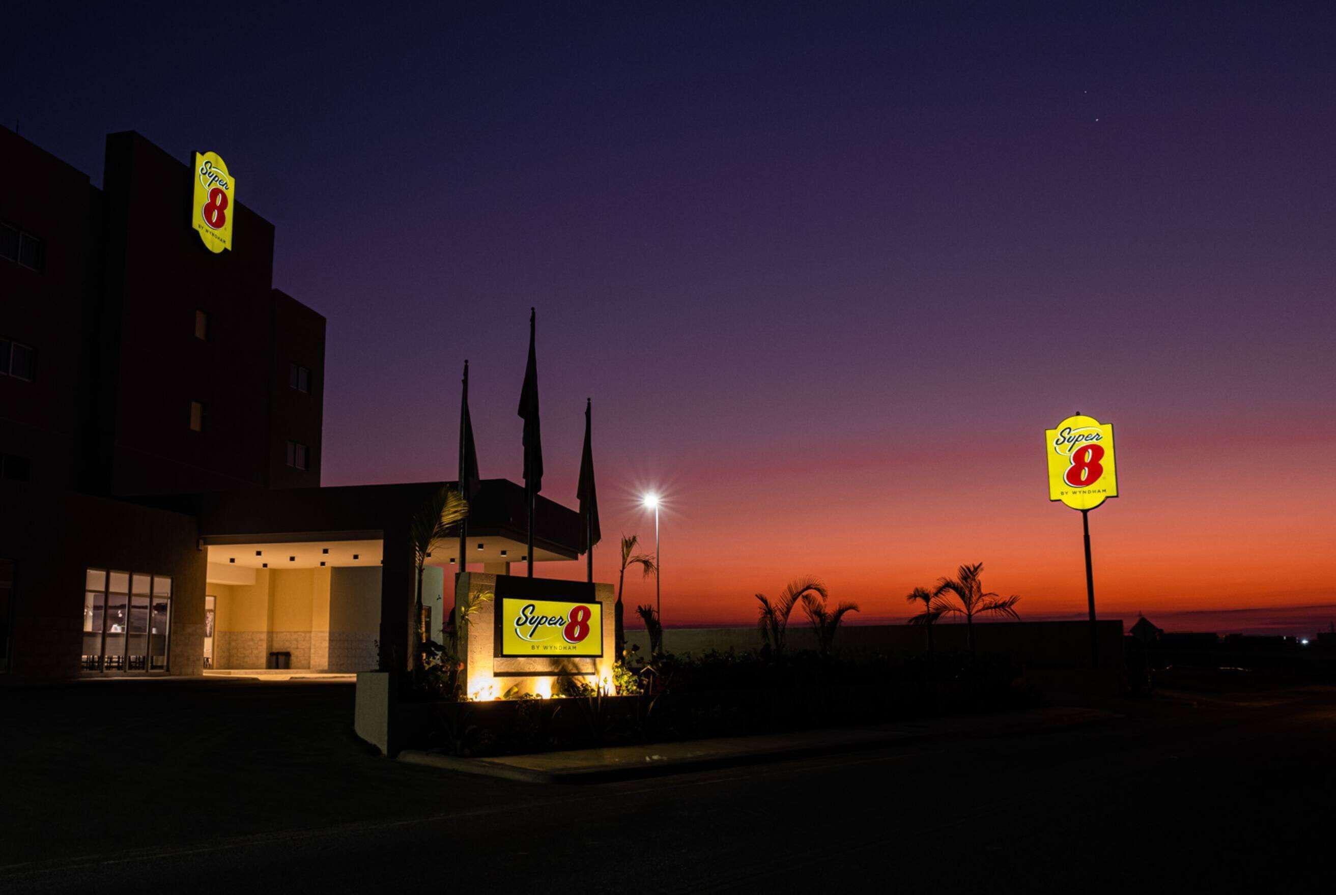 A Super 8 hotel with a prominent sign, a well-lit entrance, and a view of the sunset.
