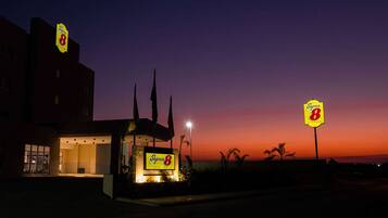 A Super 8 hotel with a prominent sign, a well-lit entrance, and a view of the sunset.