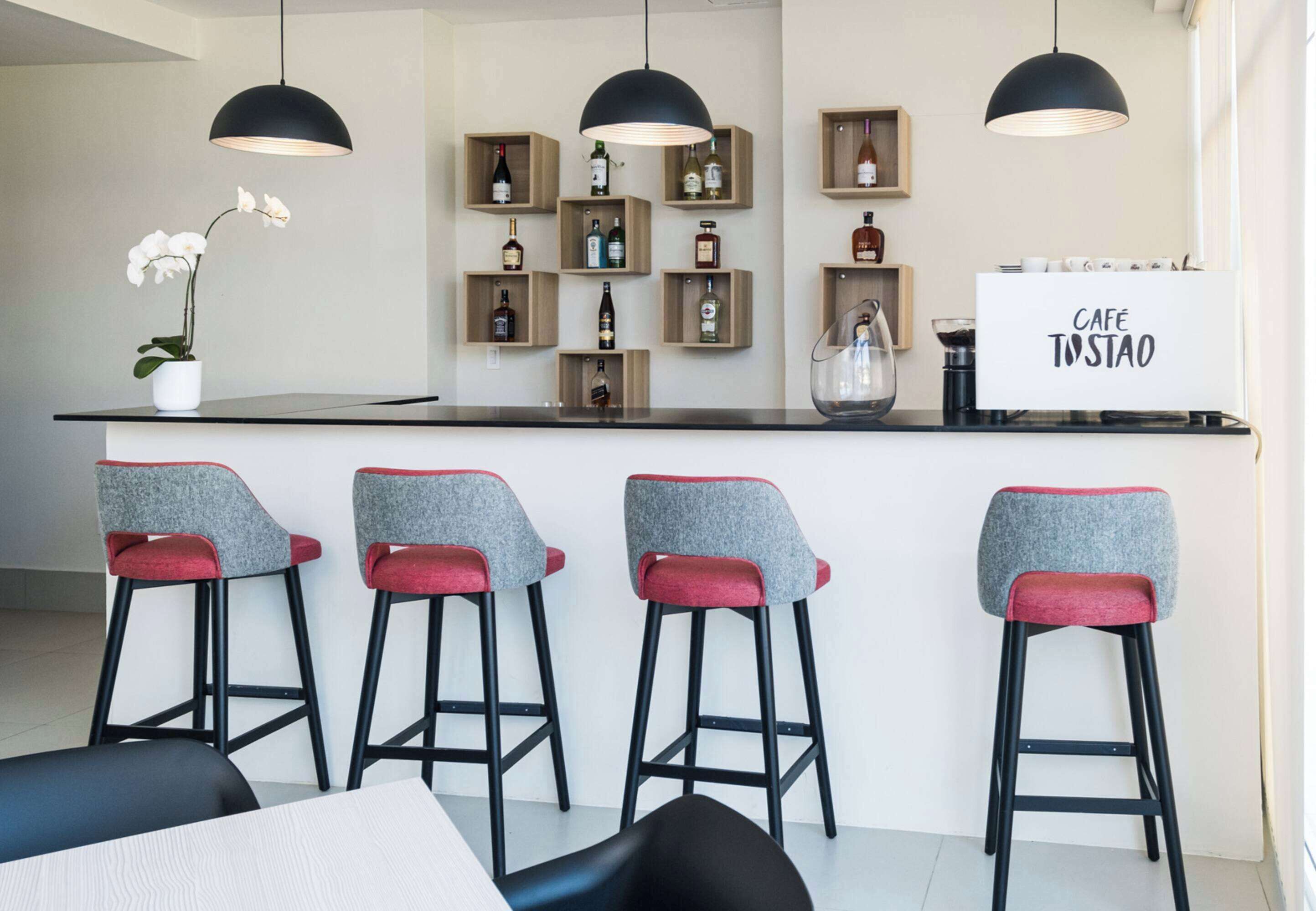 Zona de bar moderna amb un mostrador, tamborets i un expositor de licors penjat a la paret.