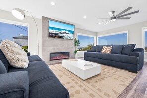 A modern living room with a fireplace, two dark sofas, a white coffee table, and a ceiling fan. - Newly Remodeled Mansion With Breathtaking 300° Views! AC, Parking, Spacious! (San Diego)