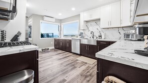 A modern kitchen with dark cabinets, white countertops, and a large window offering a view.