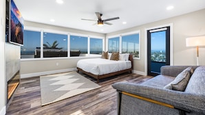 A bedroom with a large bed, a view of the city, a ceiling fan, and a window.