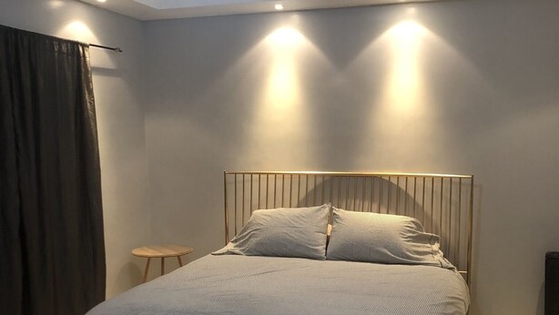 Een moderne slaapkamer met een groot bed, een klein nachtkastje en een hoofdbord met ingebouwde verlichting.