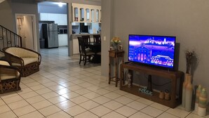 Een woonkamer met een televisie, een eethoek en een keuken op de achtergrond.