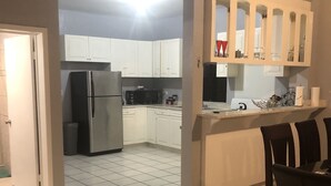 Een keuken met witte kastjes, een koelkast en een eethoek met een tafel en stoelen.