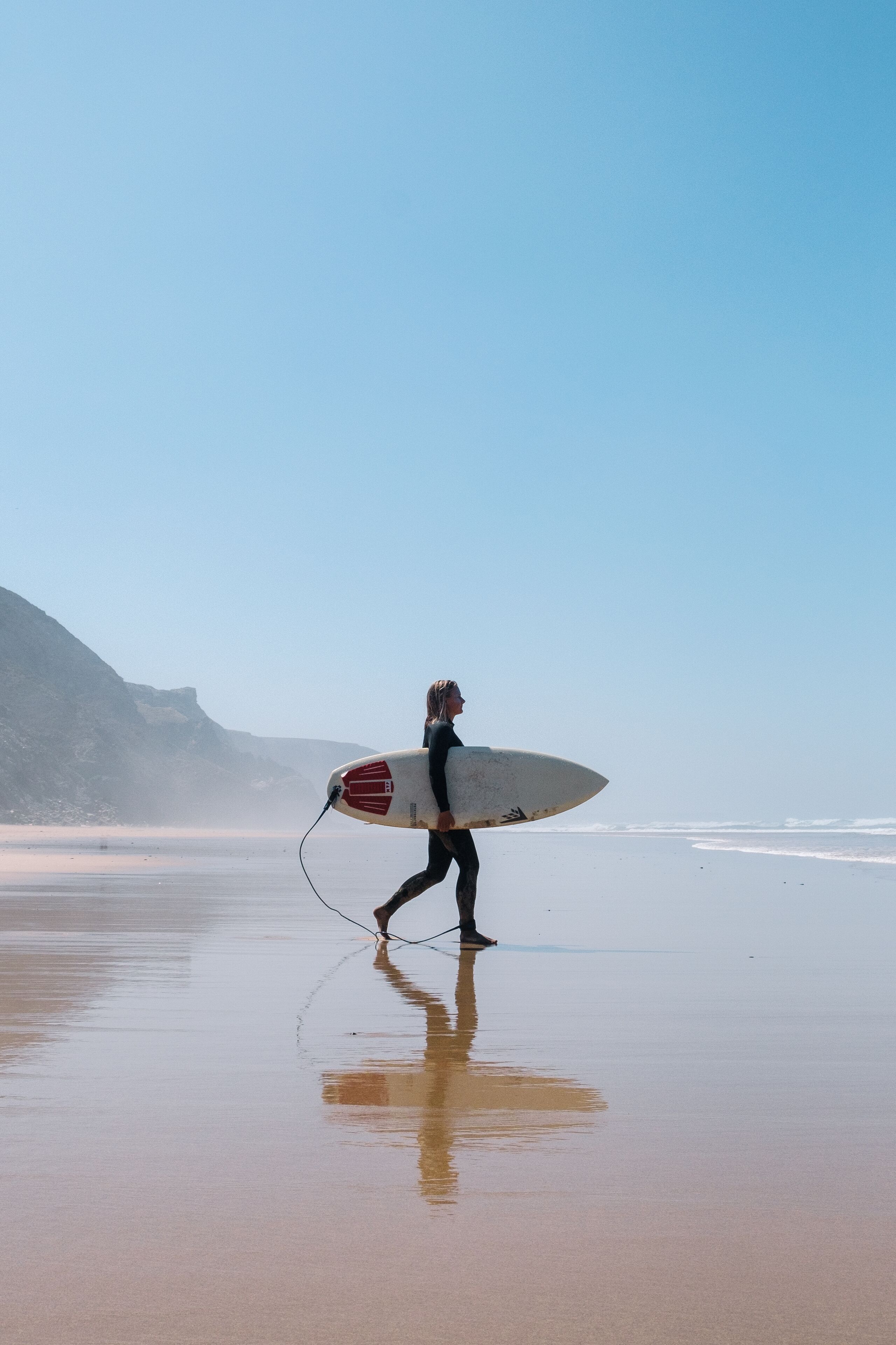 A person walking on a beach holding a surfboard.