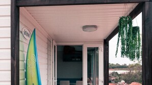 A wooden deck leading to a covered porch with a surfboard leaning against the wall.