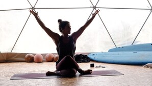 A person sitting on a yoga mat in a room with exercise balls and a blue mat on the floor.