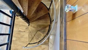Un escalier en colimaçon avec des marches en bois et des rampes en métal, menant à l’étage supérieur.