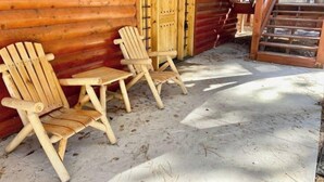 Une cabane en rondins avec deux fauteuils Adirondack à l’extérieur, un escalier en bois et une véranda couverte.