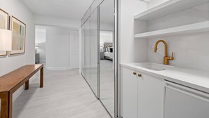 Un bagno moderno con un lavandino bianco, un rubinetto dorato e una panca nel corridoio.