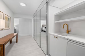 A modern bathroom with a white sink, gold faucet, and a bench in the hallway.