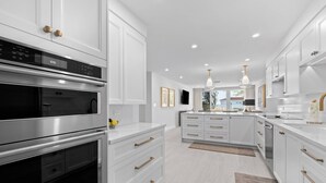 Una cucina moderna con mobili bianchi, elettrodomestici in acciaio inossidabile e lampade a sospensione.