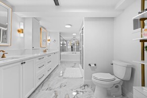 A modern bathroom with a white marble floor, a white toilet, a large mirror, and a vanity with gold fixtures.