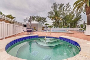 A swimming pool with a tiled edge, a lounge area with chairs, and a covered structure in the background.