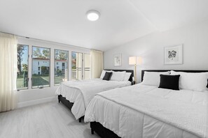 A hotel room with two beds, large windows, a ceiling light, and artwork on the walls.