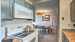 Una cocina equipada con microondas, estufa y encimeras de granito. Hay un comedor con una mesa y sillas.