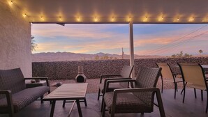 Een terras buiten met rieten meubilair, een stenen muur en uitzicht op bergen.
