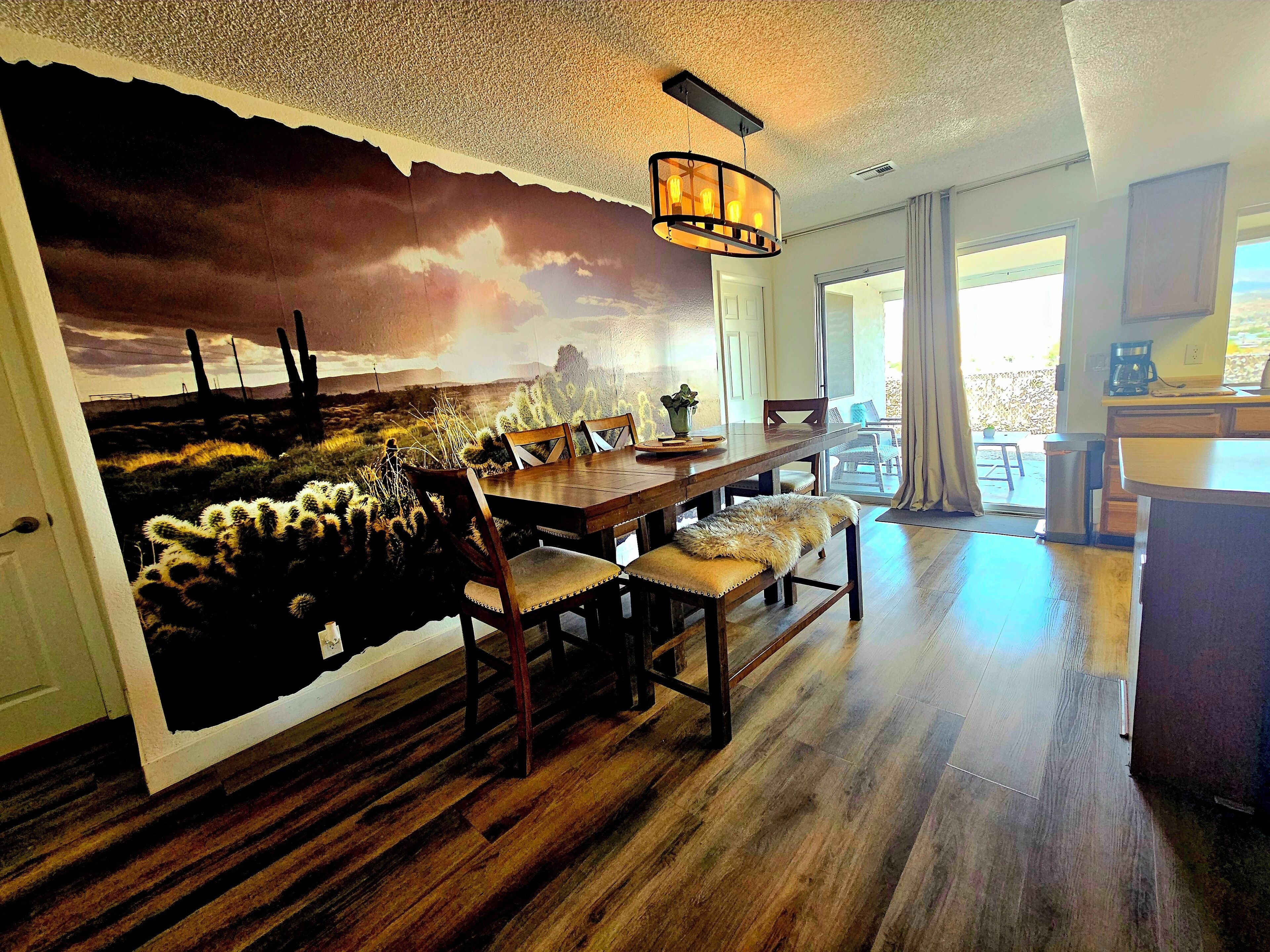 A dining area with a mural of a desert landscape, wooden furniture, and a hanging light fixture.