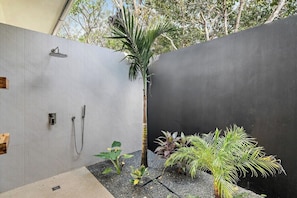 A modern bathroom with a shower, a small plant, and a concrete floor. - Casa Ola Aloha (Tamarindo)