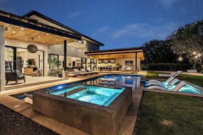 Una casa moderna amb piscina, zona d'seients exteriors i un porxo cobert.