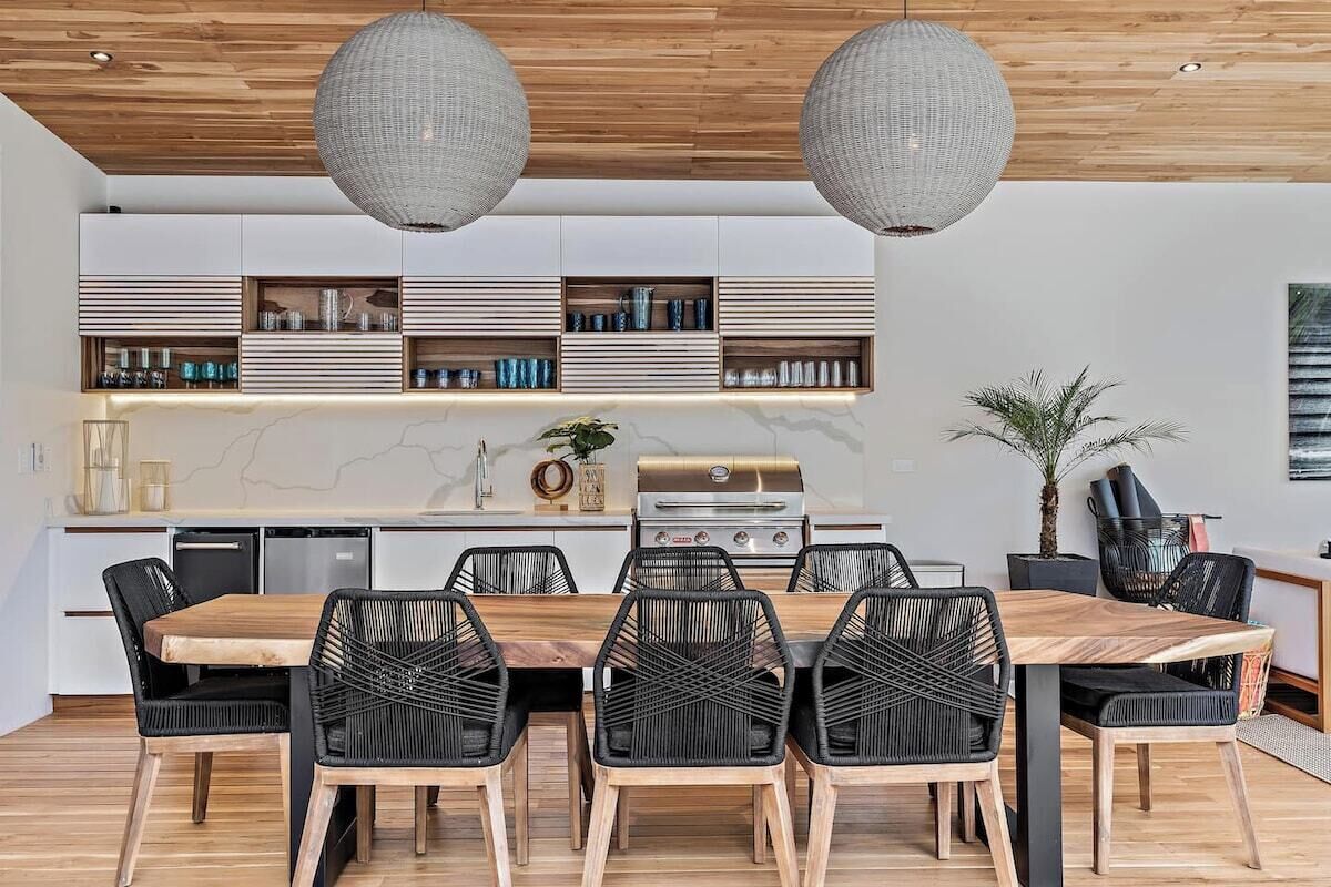 Une cuisine moderne avec une table à manger en bois, des chaises noires et un barbecue encastré.
