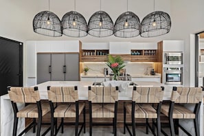 A modern kitchen with a central island, pendant lighting, and a dining area with chairs.